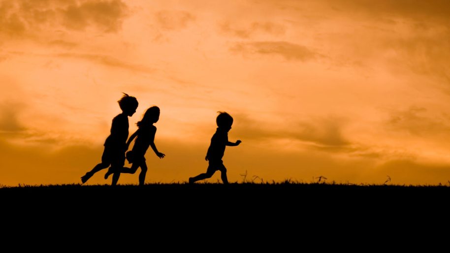 Trois enfants courent en silhouette sur une colline, au coucher du soleil.